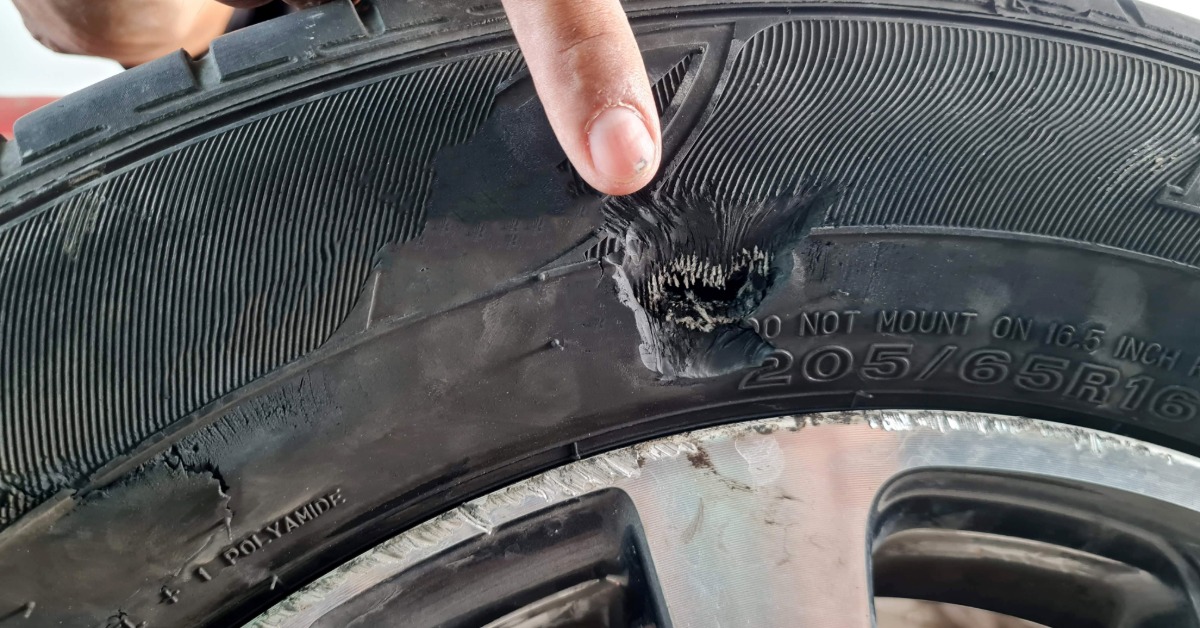 A person's hand pointing to a tear in the sidewall of a tire. The tear does not show the inside of the tire.