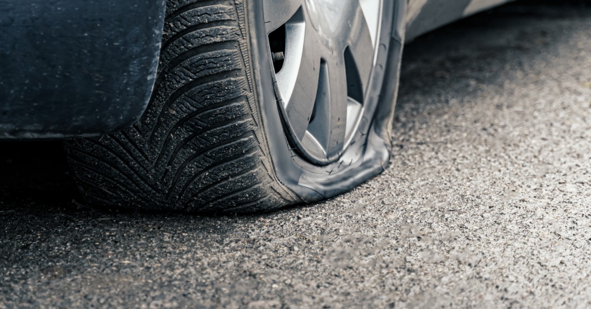 A close-up of a modern blue car with a wheel with silver rims and a punctured tire on black pavement.