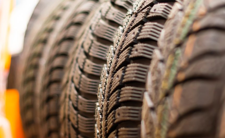 A close-up of several winter tires resting on a rack with the background blurred. The tires have deep tread blocks.