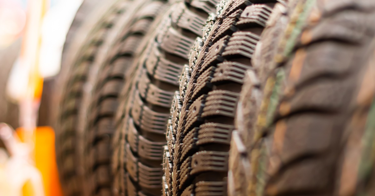 A close-up of several winter tires resting on a rack with the background blurred. The tires have deep tread blocks.