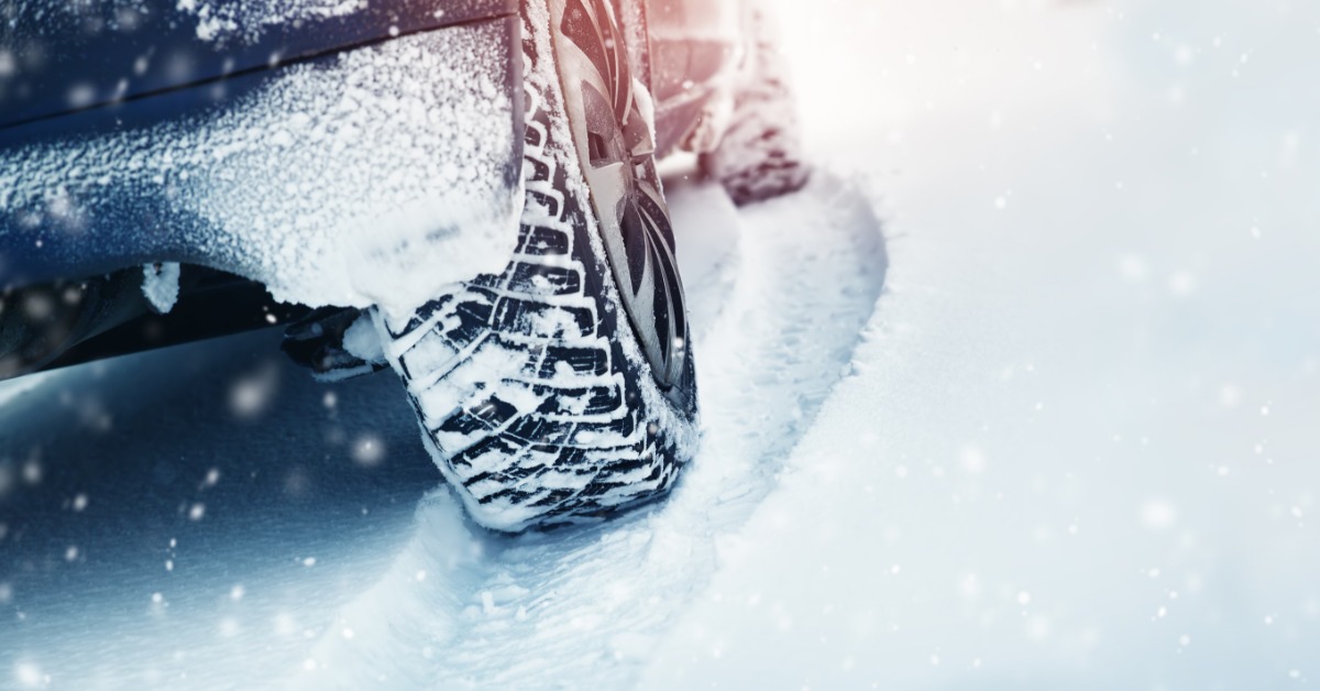 A close-up of the back right tire of a vehicle in the winter. The tire's treads are packed with snow.