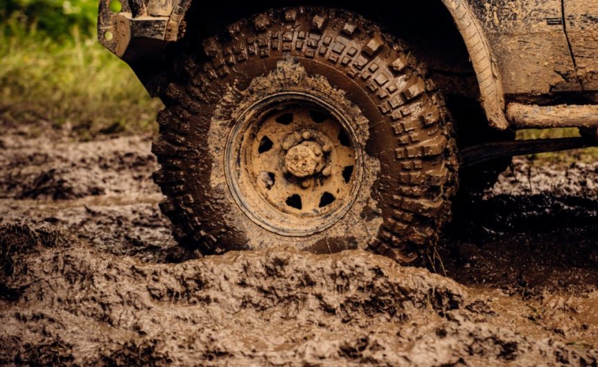 A close-up of a truck's tire in a muddy pit. The entire tire is caked in mud, including the side of the vehicle, too.