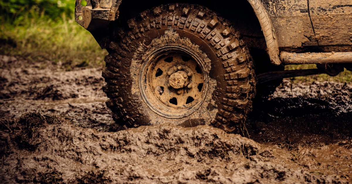 A close-up of a truck's tire in a muddy pit. The entire tire is caked in mud, including the side of the vehicle, too.