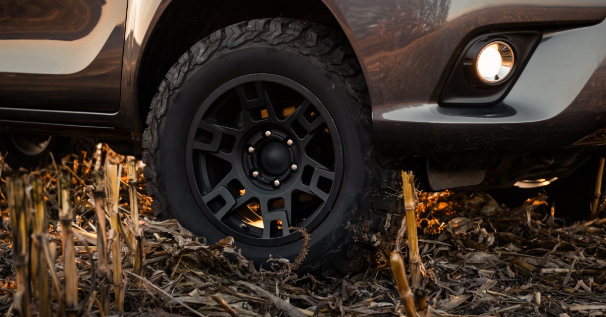 A close-up of the side of a shiny truck parked in a harvested corn field. The front off-road tire is brand new.