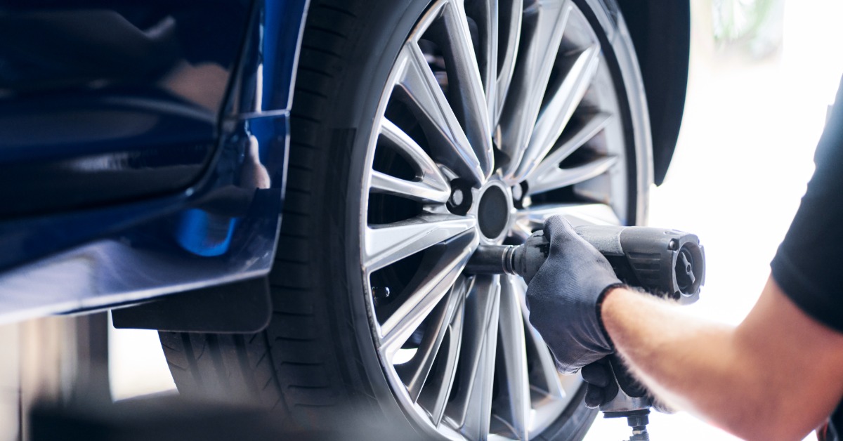 A close-up of a mechanic using a pneumatic wrench to remove the lug nuts from the wheel of a car on a lift.
