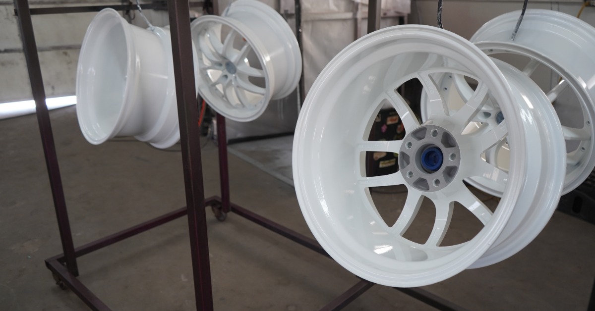 Four automotive wheels with white powder coating finishes hanging from hooks on a standing rack in a garage.