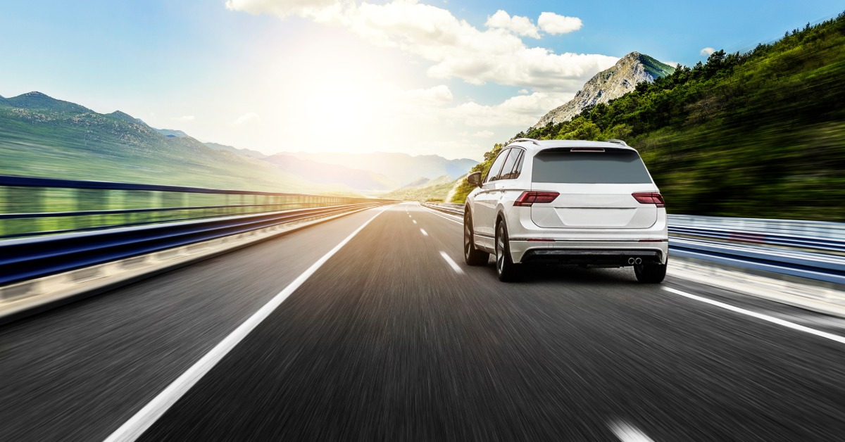 A white SUV is driving down a highway in the right lane. The sides of the road are slightly blurred as the car drives by.