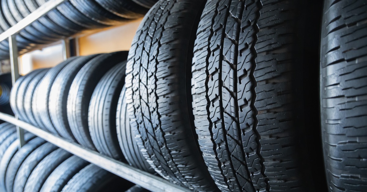 A long row of black car tires with deep tread patterns. All of the tires are clean, and there are three rows of shelves.