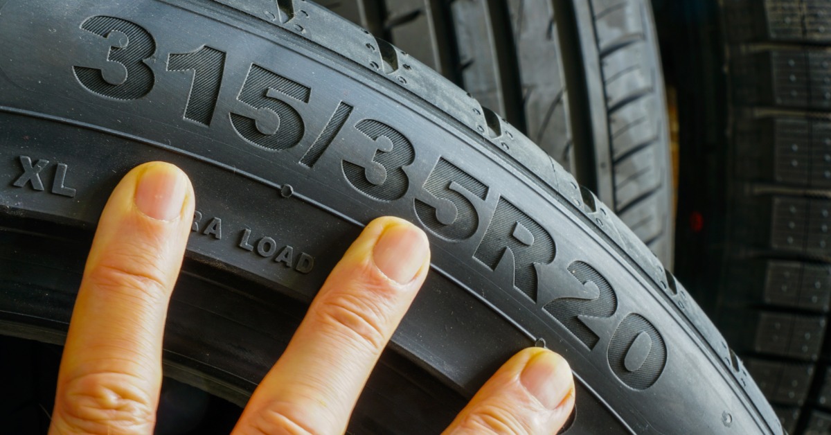 A close-up of the sidewall of a tire with the numbers "315/35R20" and a person's three fingers for size comparison.