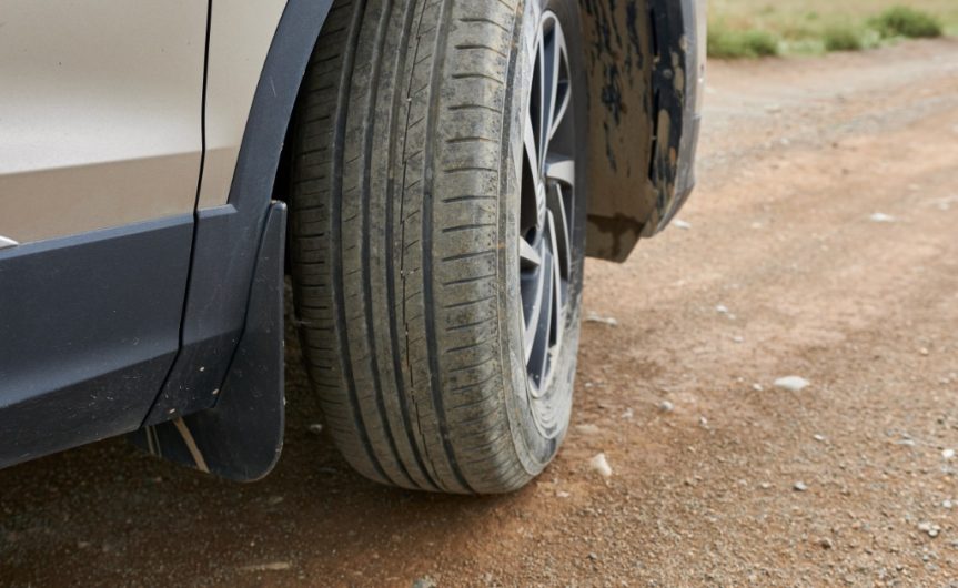 A car with the wheel turned slightly inward towards the vehicle. The car is parked on an empty dirt road.
