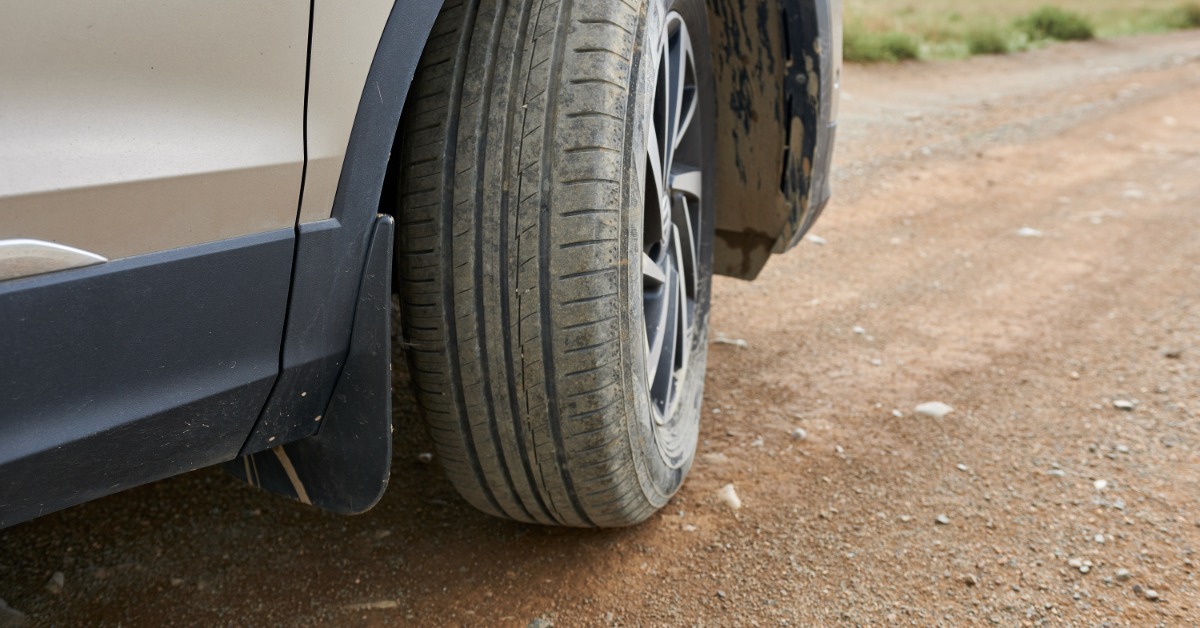 A car with the wheel turned slightly inward towards the vehicle. The car is parked on an empty dirt road.