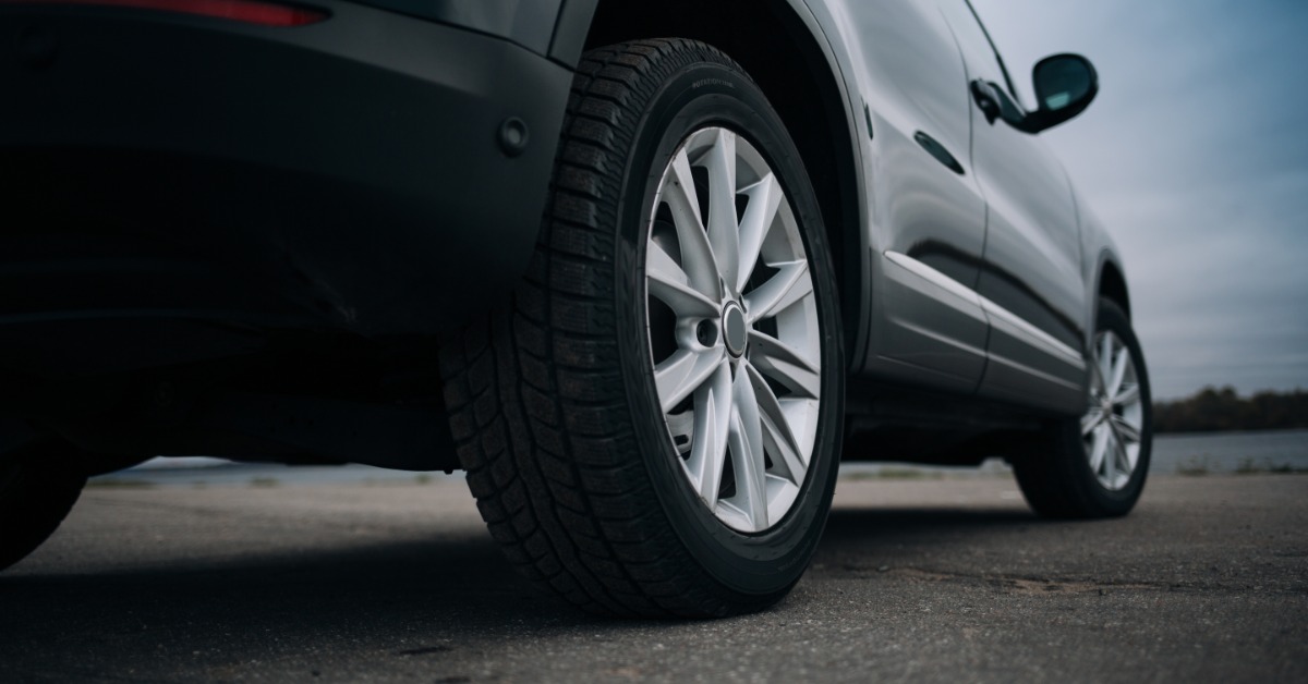 The rear wheels of a black SUV are parked on the pavement. The wheels and exterior of the vehicle are clean.