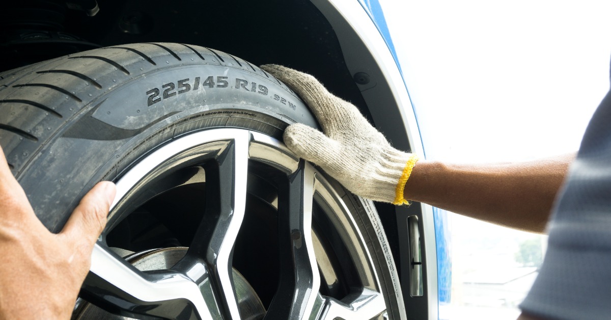 A man's hands with gloves holding a tire into the wheel position with the tire size numbers and load index numbers visible.