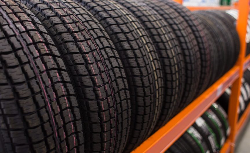 A close-up of a two-level orange rack holding brand-new automotive tires for sale displayed vertically.