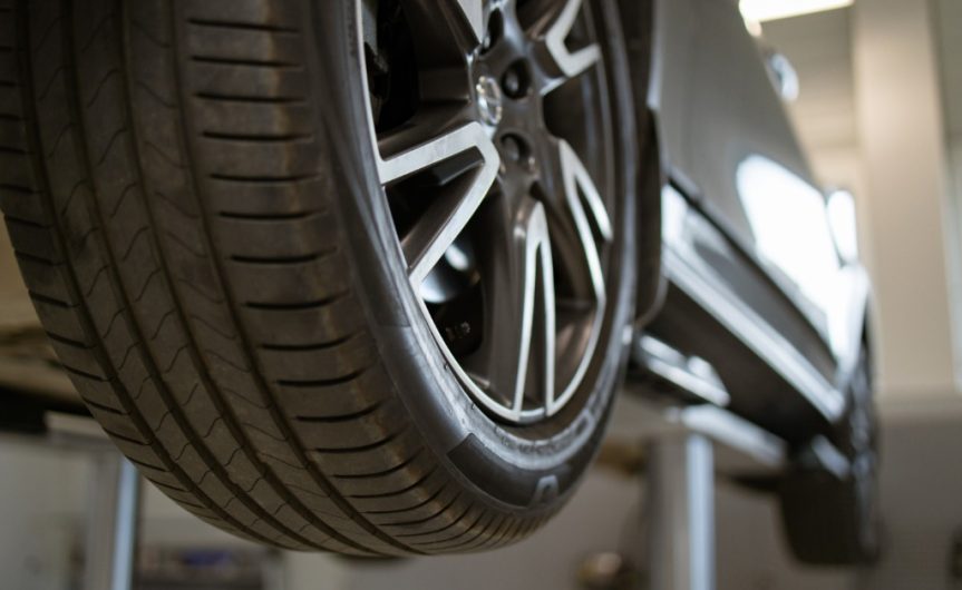 A close-up of a car tire on a vehicle lift inside an auto repair shop. The tread pattern is visible.