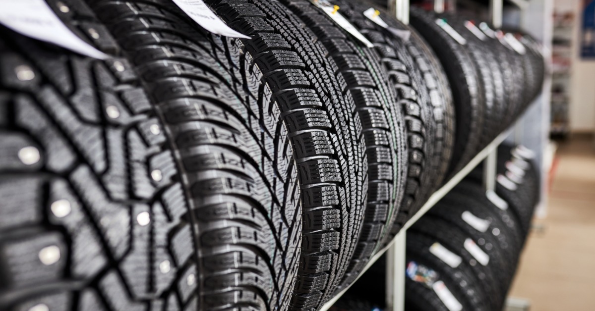A wall of brand-new tires with deep tread patterns in an auto shop. Each tire has a tag on it with extra details.