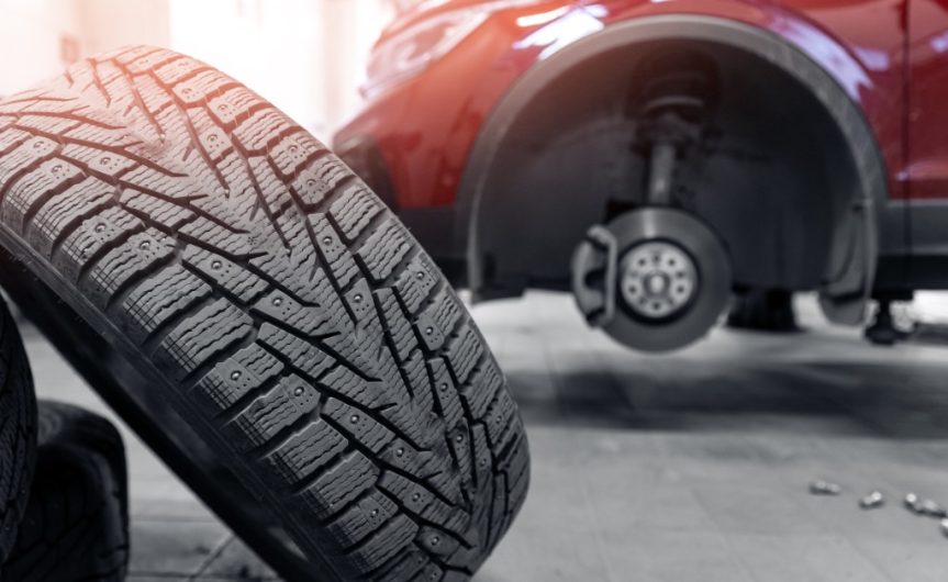 A close-up of used car tires stacked together in a pile with a red modern car without wheels on a lift.