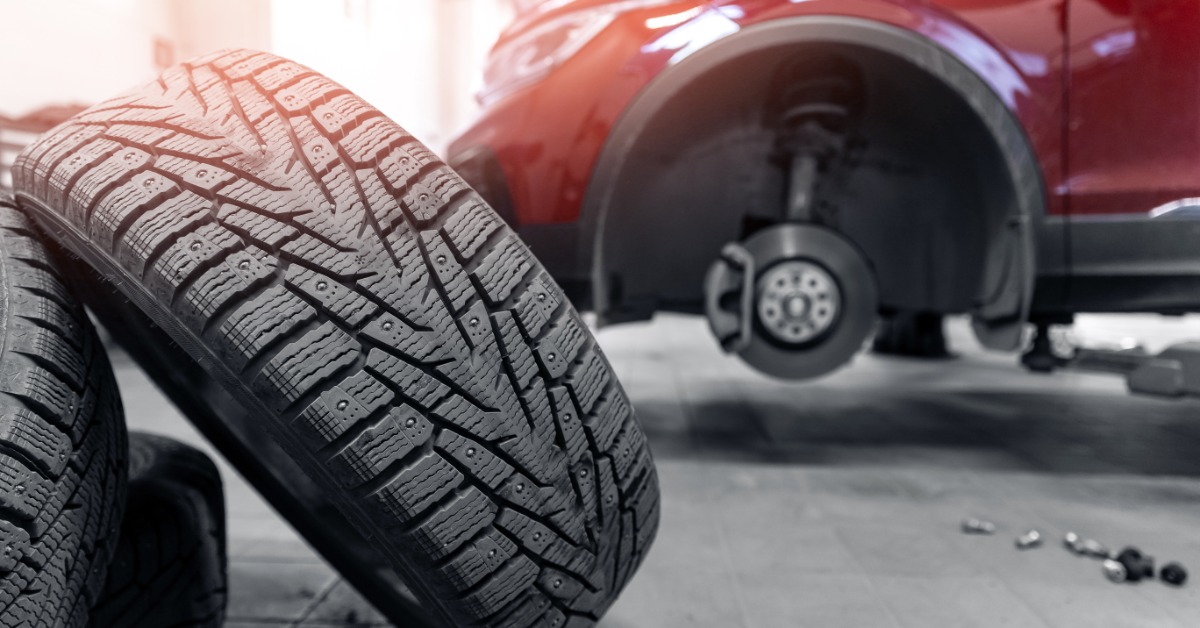 A close-up of used car tires stacked together in a pile with a red modern car without wheels on a lift.