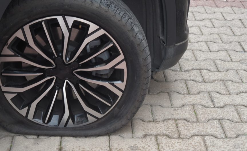 A flat tire attached to a black vehicle. The tire and wheel are clean, but the tire has insufficient air.