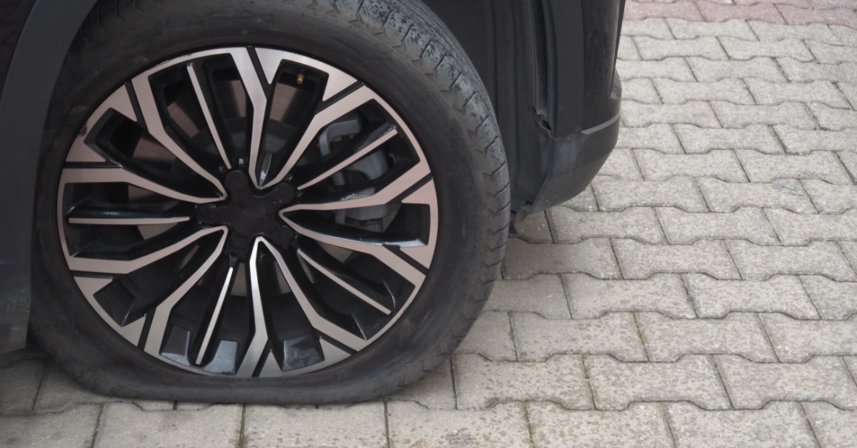 A flat tire attached to a black vehicle. The tire and wheel are clean, but the tire has insufficient air.