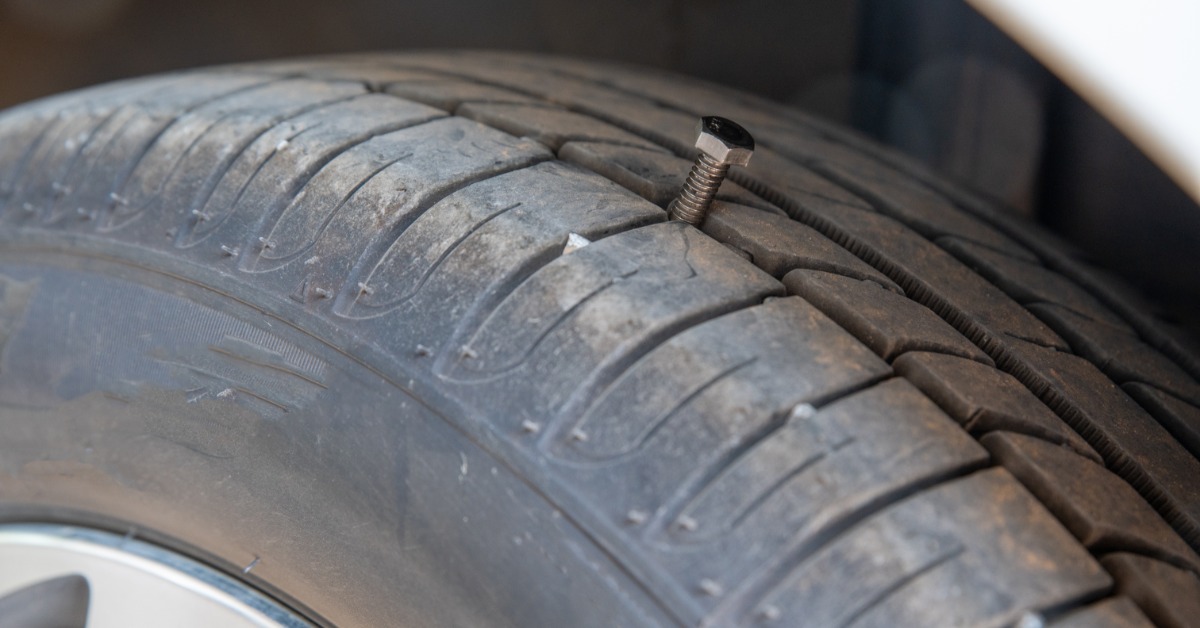 A tire attached to a car with small dust on it. There is a nut in the middle of the tread, damaging the tire.