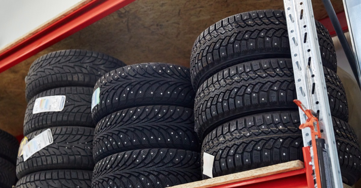 Three stacks of tires on the top shelf of a red shelving unit. A few of the tires have a tag on them.