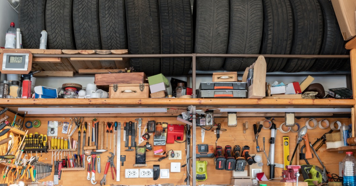 A garage with a workbench spanning across a wall. Tools are hung up with tires on a rack above the workbench.