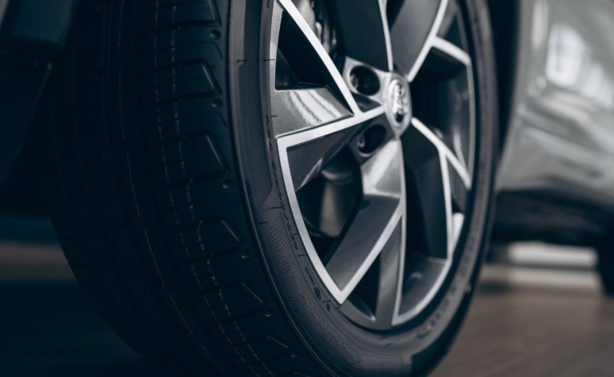 A close-up of the back tire of a vehicle with the car blurred. The tire is brand new with shiny silver rims.