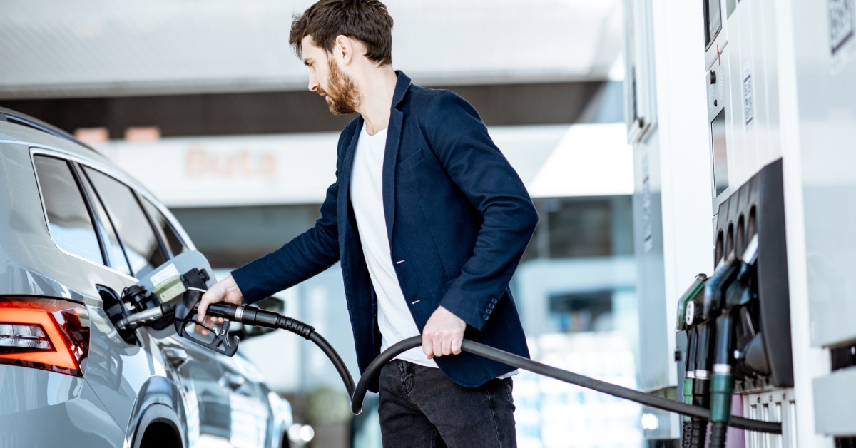 A man stands between his vehicle and a gas pump. He is inserting the nozzle into the car's gas tank.