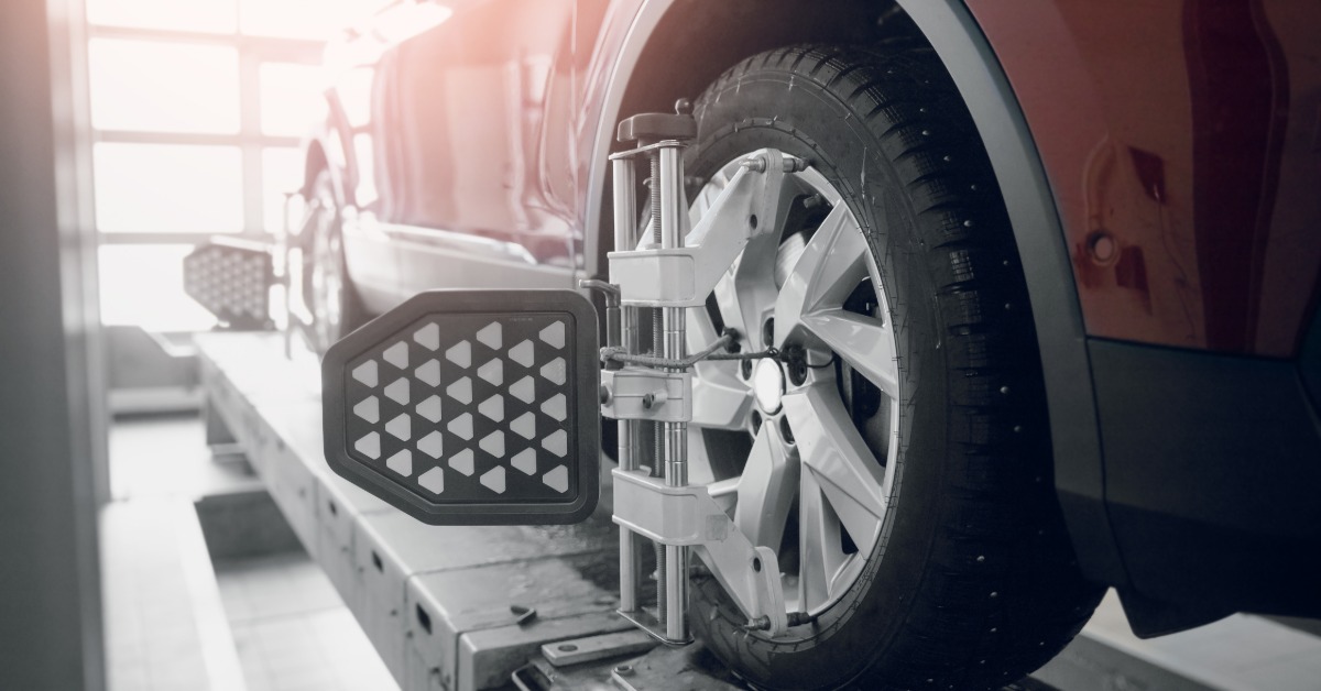 A close-up of the back tire of a red car on a lift in an auto shop. Wheel-alignment targets are attached to the front and back tires.