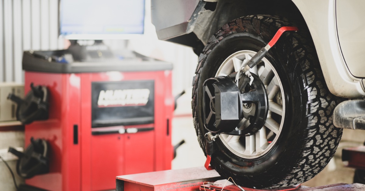 A close-up of the back tire of a vehicle on a car lift. A wheel-alignment device is attached to the back tire.