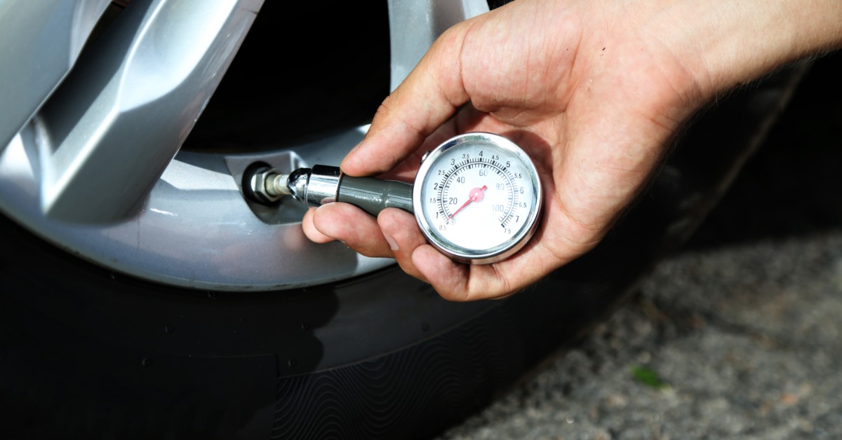 A close-up of someone holding a tire pressure gauge up to the valve of a tire. The gauge is still resting at 0 PSI.