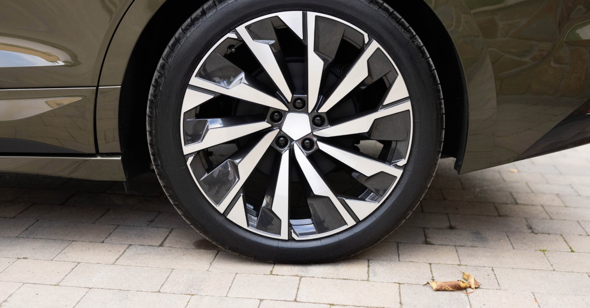 A close-up of a new tire with modern rims on an electric vehicle. The vehicle is painted a forest green.