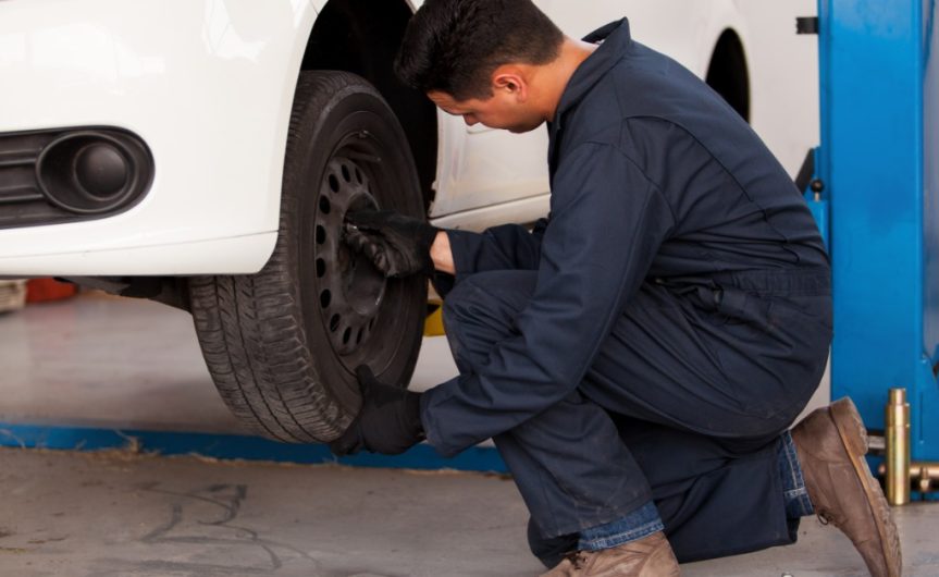 A close-up of a person's fingers pressing on the tread of a used car tire elevated on a lift in a garage.