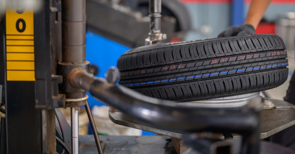 A person's hand with black gloves placing an automotive tire on a tire-rotating machine mount in an auto garage.