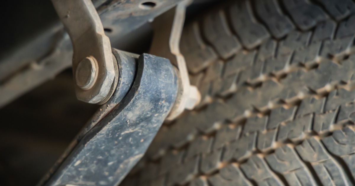 On the undercarriage of a car, the suspension of a car is dirty. The tire tread is visible behind the suspension.