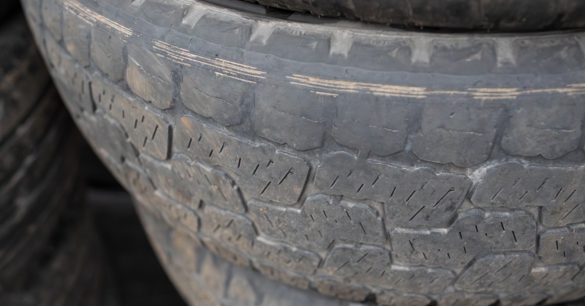 An old tire in a stack that shows visible wear and tear along one side of the tread. The tire is also dirty.