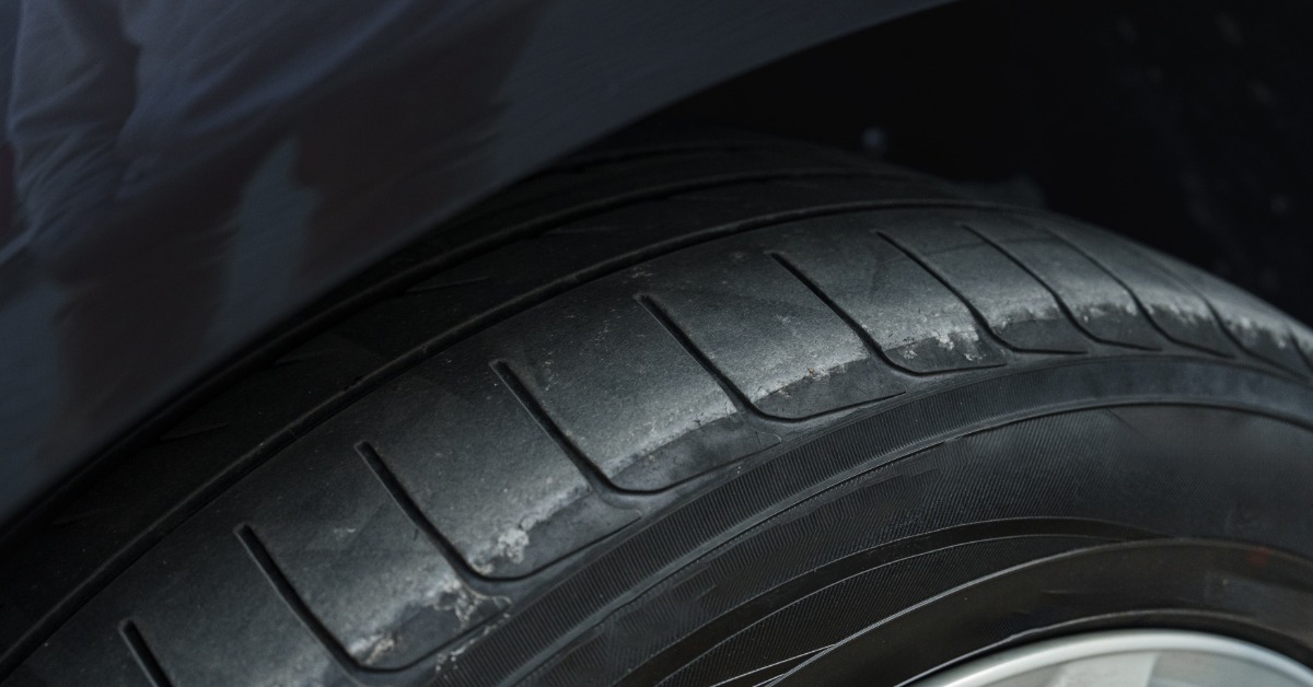 A car tire attached to a vehicle with signs of wear and tear. The tread on the tire is completely worn down.