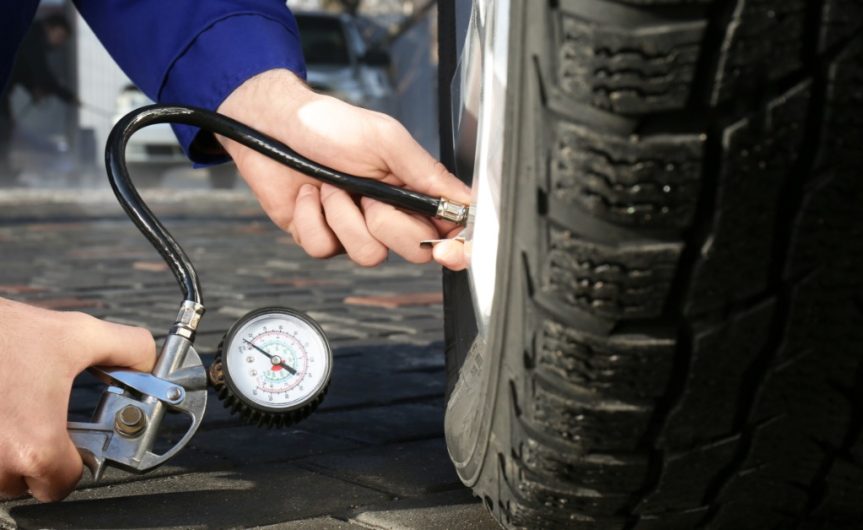 A person checking the tire pressure on a car tire with a pressure gauge. The tire is clean with no visible damage.