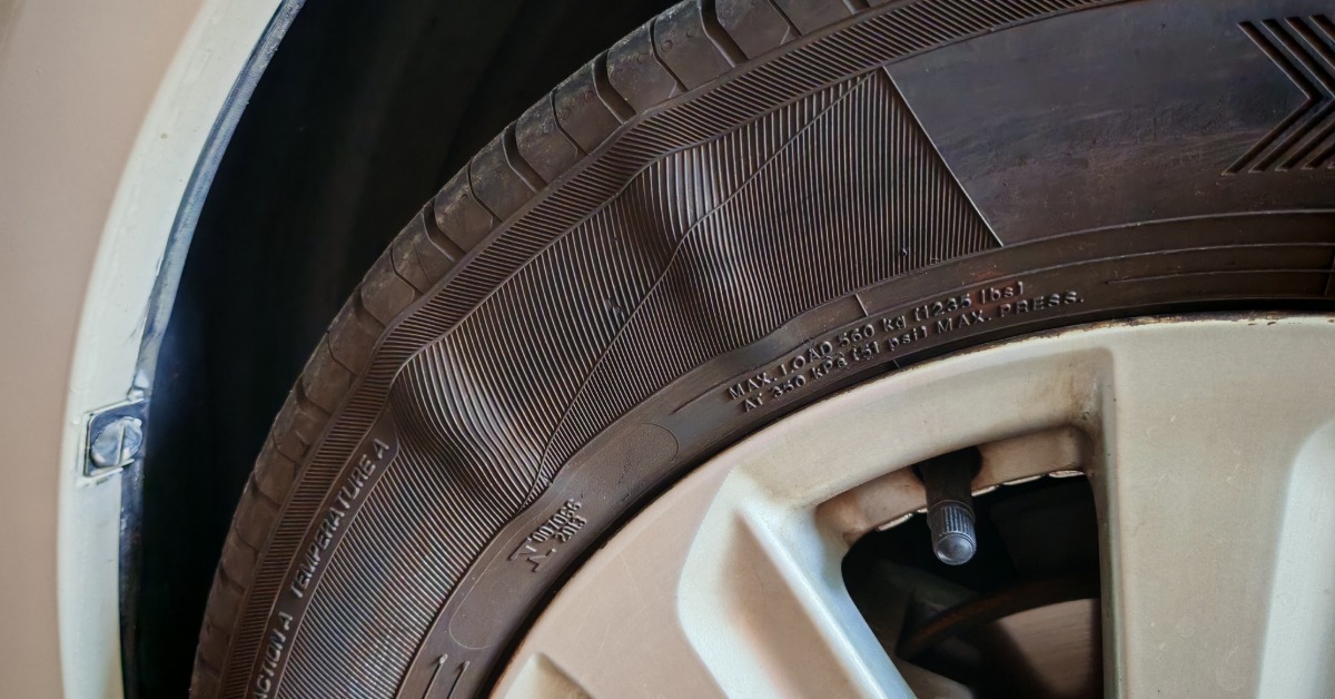A tire attached to a vehicle. The top part of the tire has two bulges in the sidewall, which indicates damage.