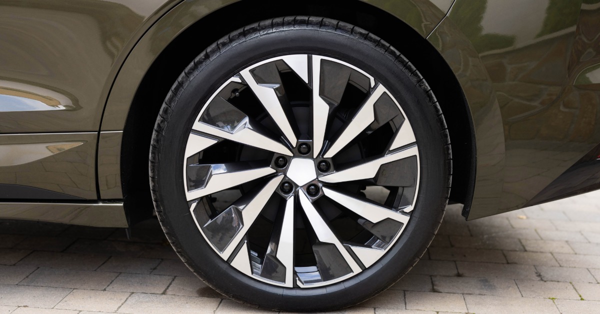 The rear tire of a modern vehicle parked on a clear road. The tire is clean and has no visible wear.
