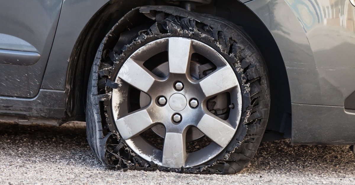 A tire blown out on a grey vehicle. The tire is completely ripped apart, with the car resting on the rim.
