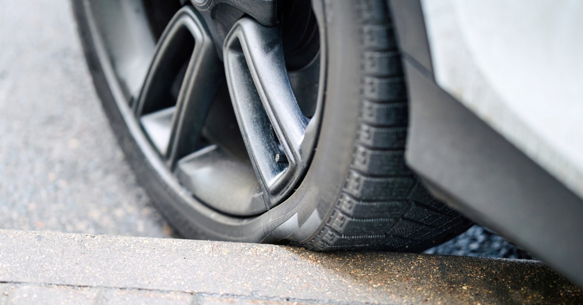 A close-up of a tire hitting the curb on some sidewalk. The tire is dented slightly where it meets the pavement.