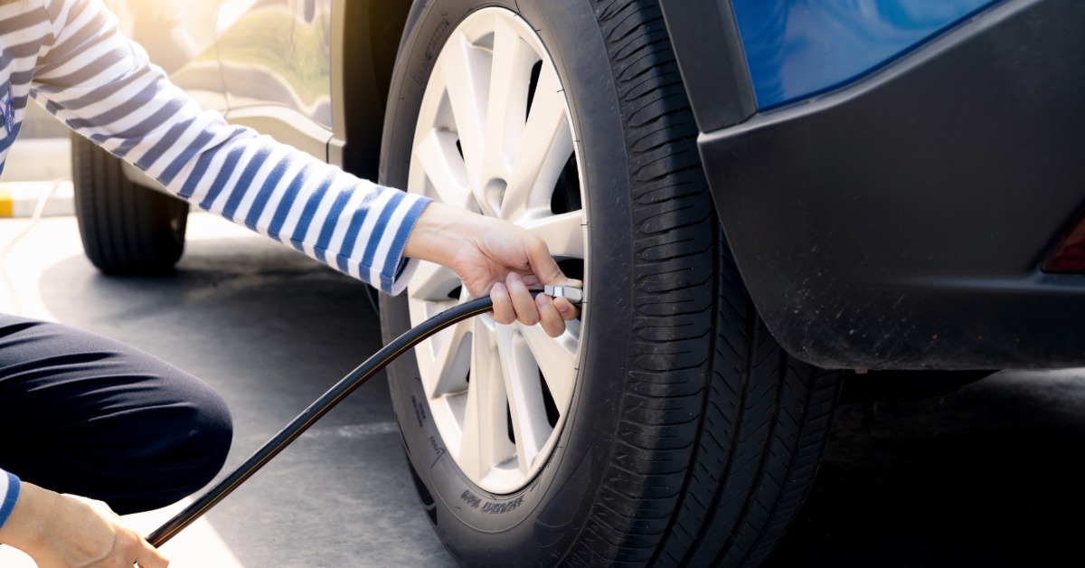 A woman holding a tire pump on the tire valve to inflate it. She is wearing dark pants and a striped shirt.