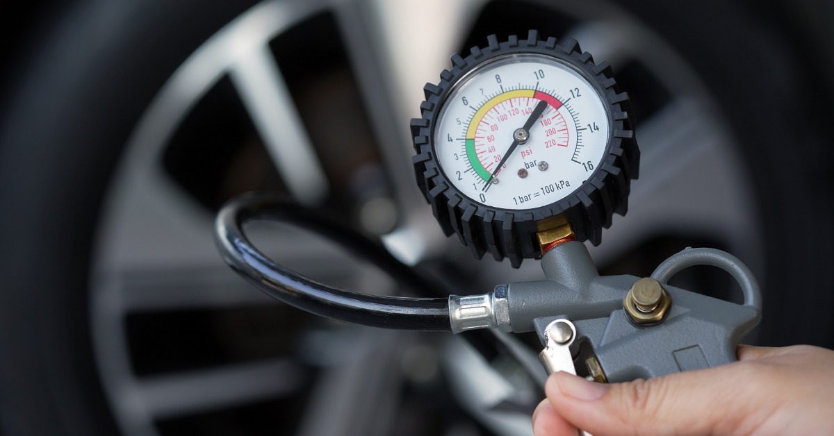A person holding a tire pressure gauge up, which is connected to the tire. The gauge shows various numbers.