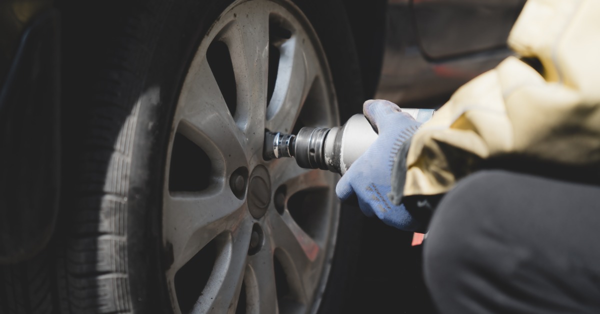 A close-up of someone wearing blue gloves using a lug wrench, loosening the lugs on a tire to remove it from a vehicle.