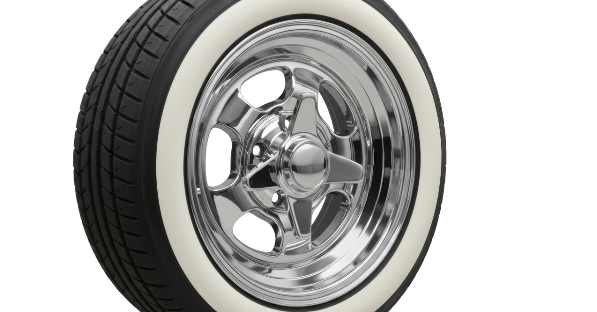 A car wheel and tire in isolation against a blank background. The wheel is chrome and the tire whitewall.
