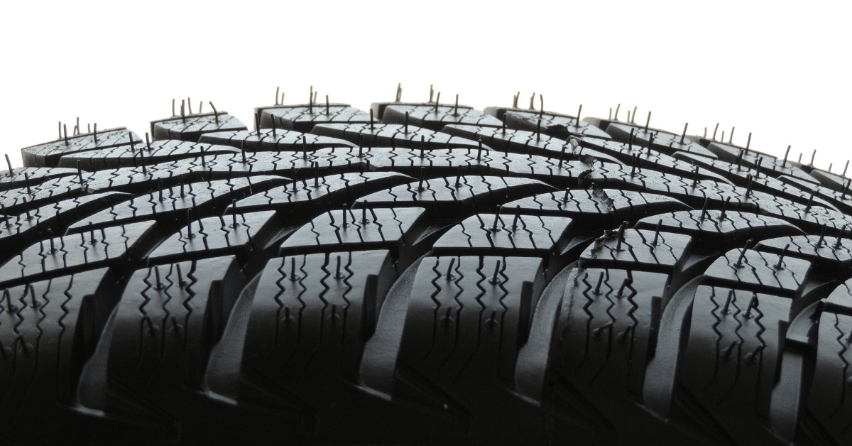 A close-up of a new automotive tire with a focus on its sipes, grooves, and tread block design against a white background.