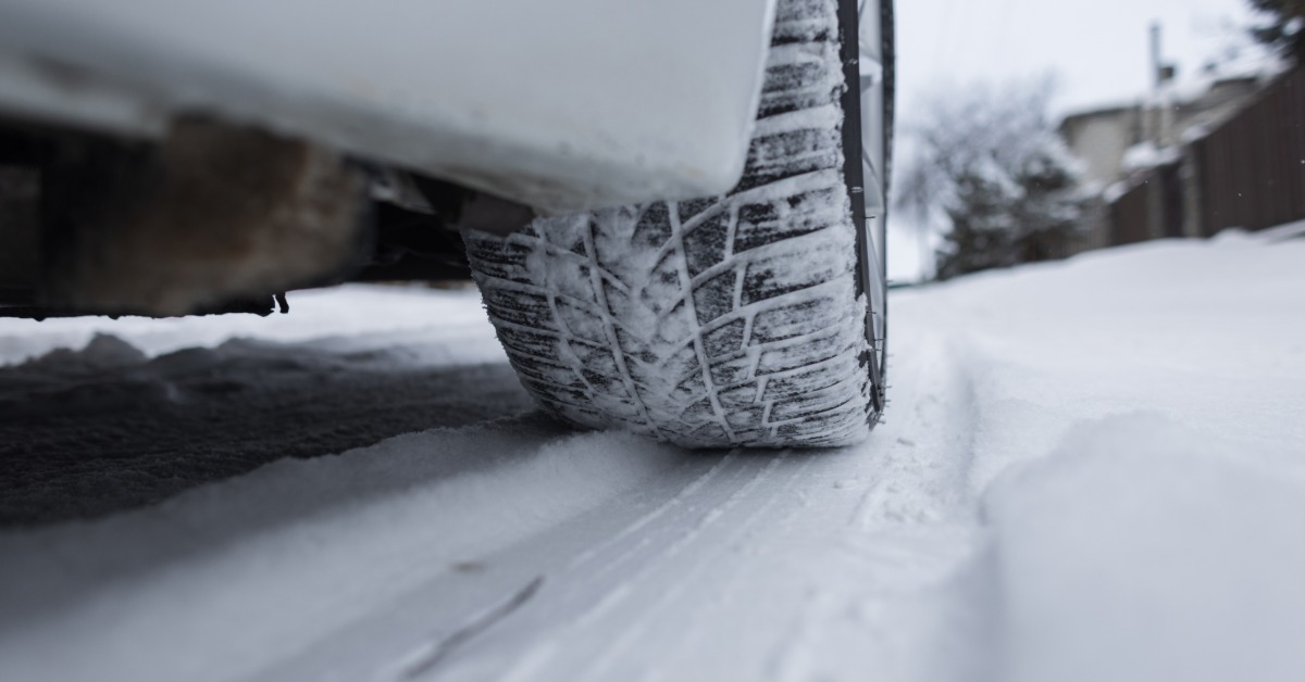 A close-up of a winter automotive tire driving on a snowy surface with snow in the tire's tread blocks.