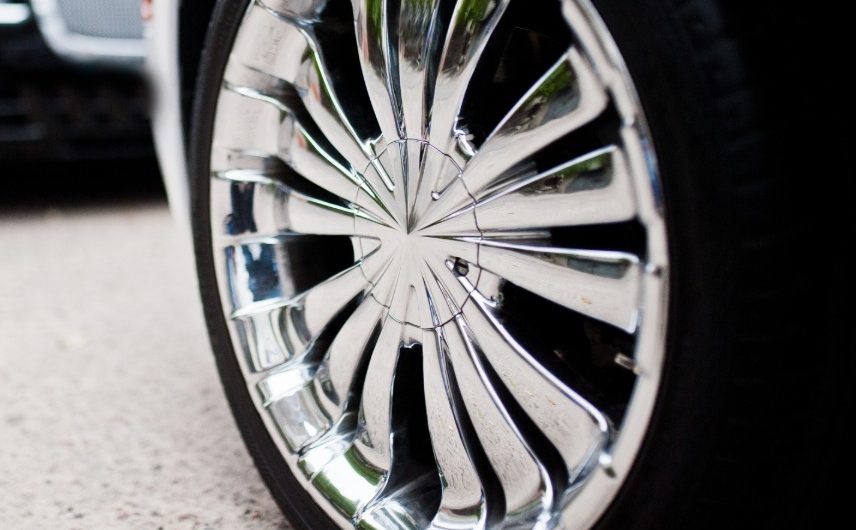 A close-up of a white car's shiny chrome wheel parked on a pavement with a black car opposite facing it.